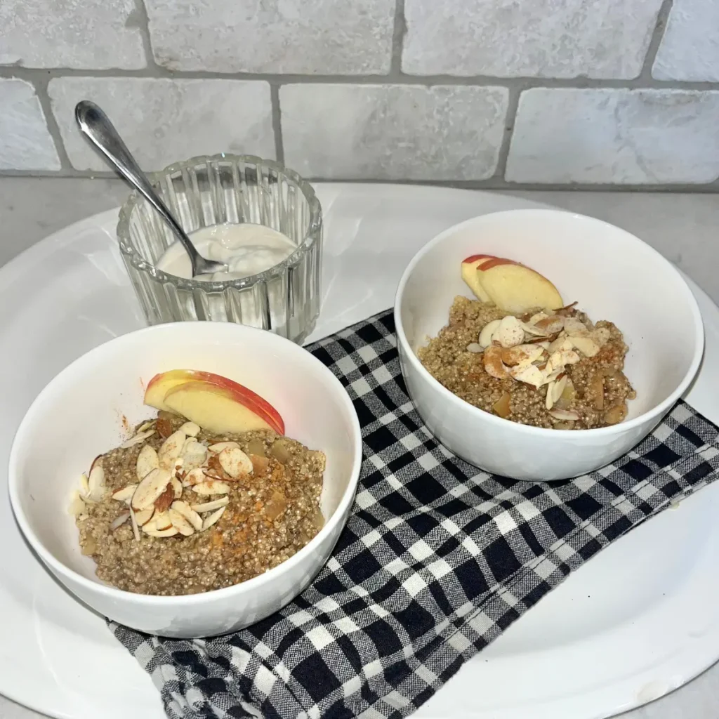 Two quinoa bowls with apple slices on top on a white platter on the counter.
