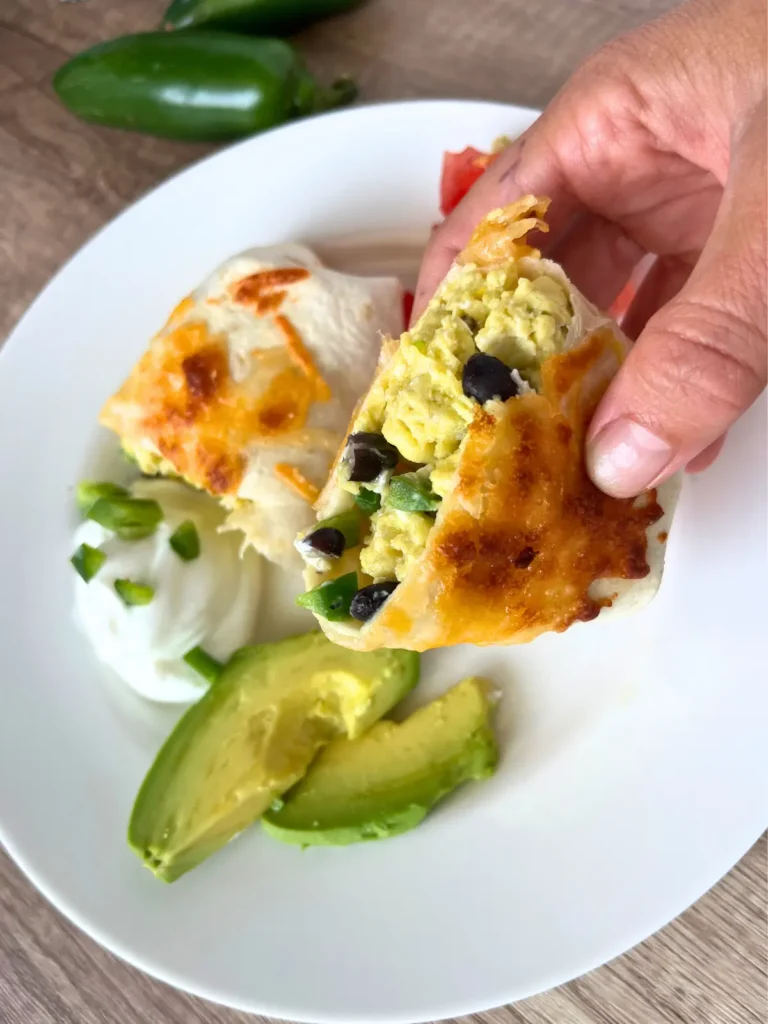 Someone holding a half of a burrito in their hand with the other half on a plate in the background.