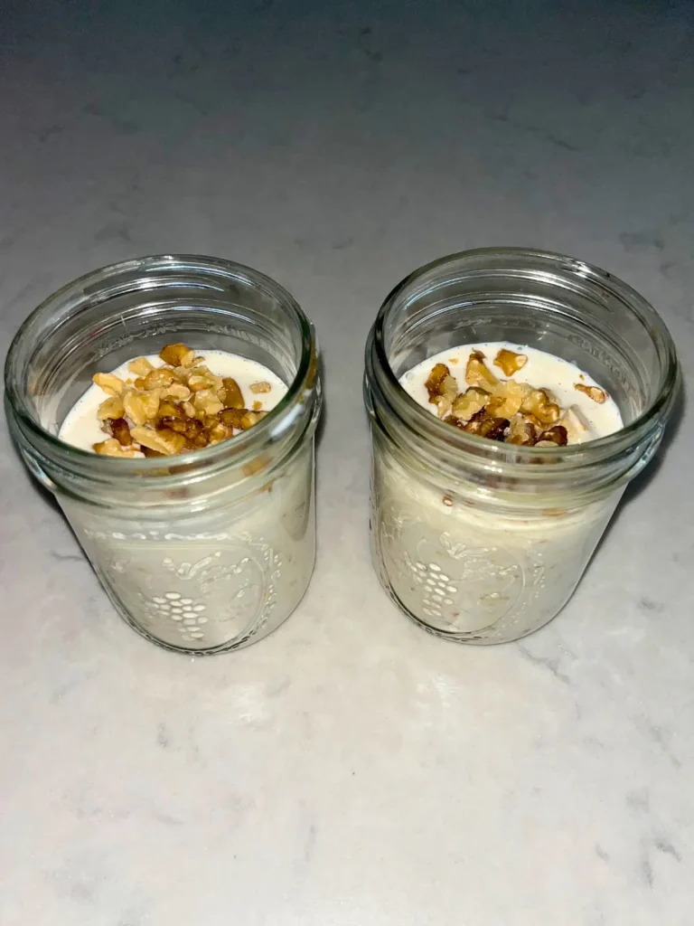 The overnight oats mixture combined with the caramelized apples in mason jars and topped with chopped walnuts, prior to refrigeration.
