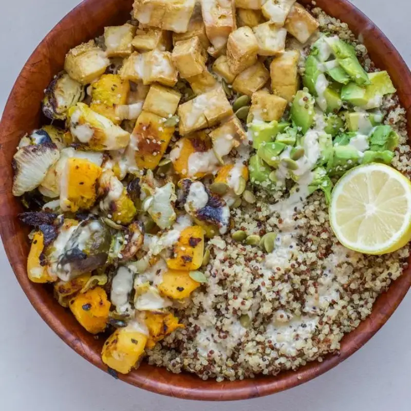 A buddha bowl with each ingredient divided and a drizzled sauce on top.