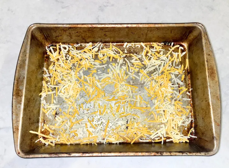 A rectangular pan with a layer of shredded cheese on the bottom for the cheese crust.