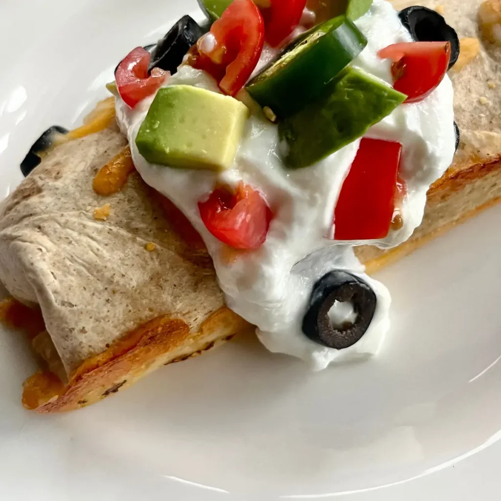 A close-up of a high protein breakfast burrito with a crispy cheese crust topped with Greek yogurt and diced jalapenos.