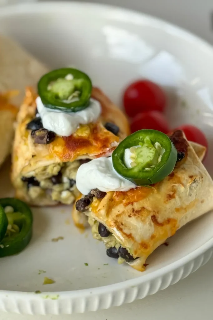 A breakfast burrito cut in half with Greek yogurt and jalapenos on top on a plate.