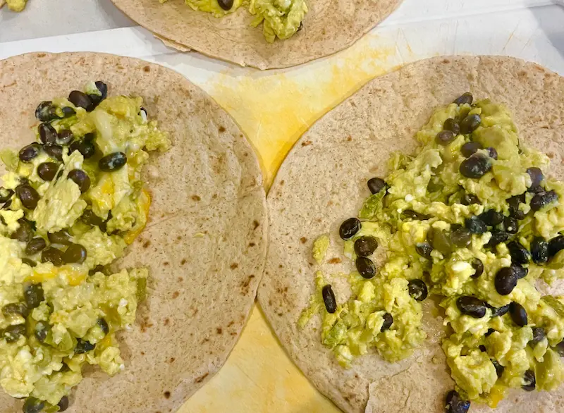 Tortillas lying flat on a clean surface with egg mixture in the middle, prior to folding.