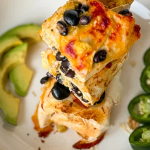 Three halves of a crispy cheese crust high protein breakfast burrito with black beans stacked on top of one another on a plate garnished with avocado slices and jalapenos.