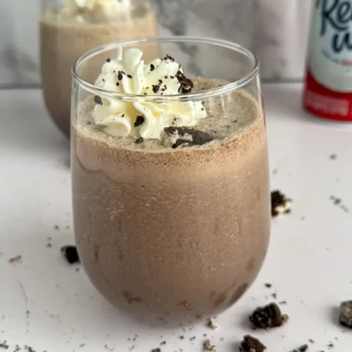 An Oreo protein shake in a glass with whipped cream and another shake in the background.
