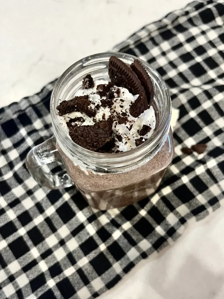 An Oreo protein shake on a counter topped with whipped cream and crushed Oreo crumbs.