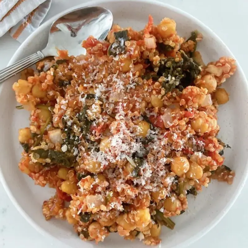 A bowl of quinoa with spinach, tomatoes and chickpeas with a little cheese topped on it.