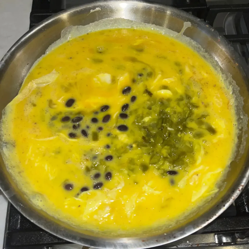 Raw eggs in a pan with black beans and diced jalapenos. 