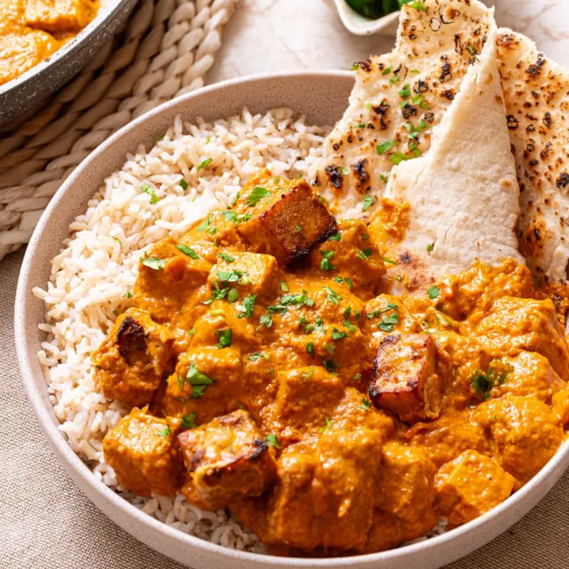 Tempeh tikka masala with rice and a side of pita bread in a large bowl.