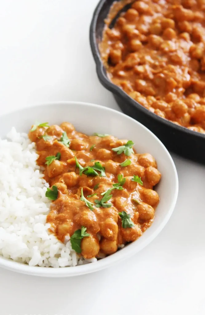 Vegan butter chickpeas with white rice in a white bowl next to a large pan.