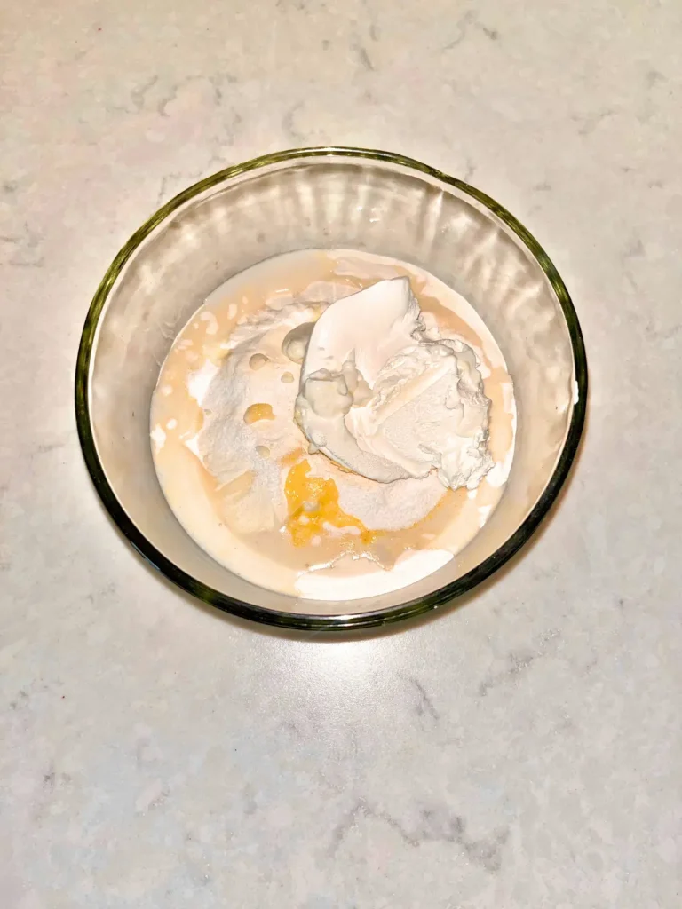 Protein powder, Greek yogurt, pudding mix, water, and vanilla extract adding to a glass bowl.