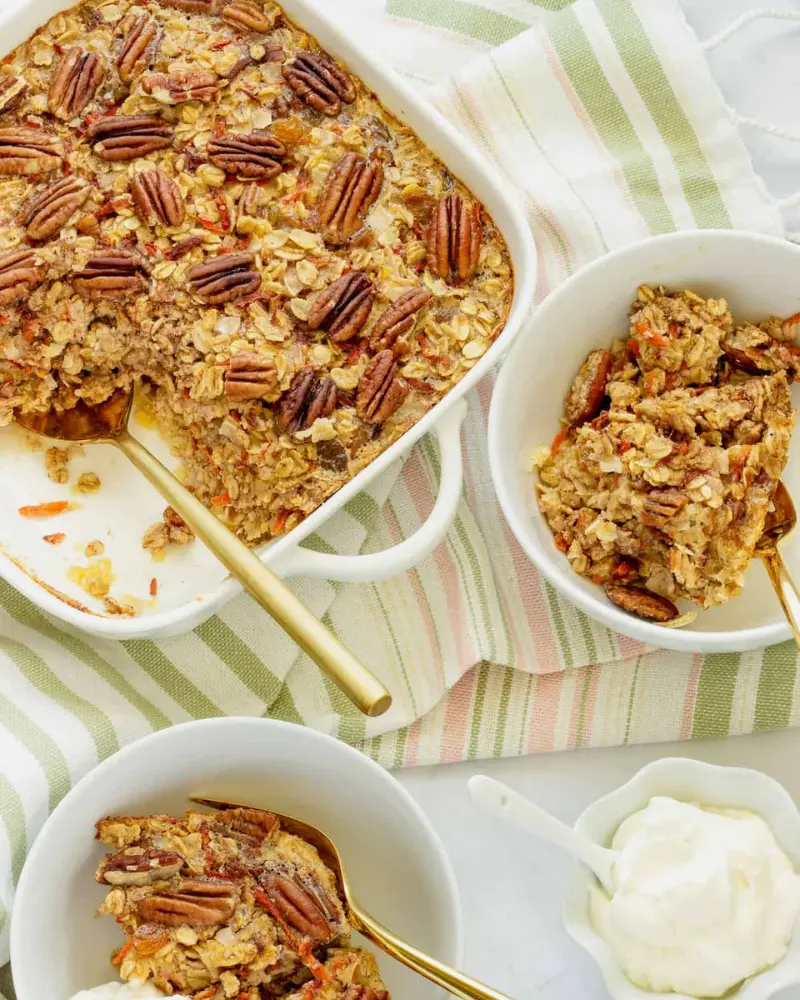 A large pan of carrot cake baked oatmeal on a table next a bowl of it with a spoon.