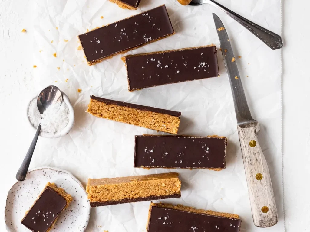 Sliced chocolate peanut butter oatmeal bars on a parchment paper lined cutting board next to a knife.