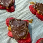 Dark chocolate strawberry bark pieces on a white platter - some drizzled with peanut butter.