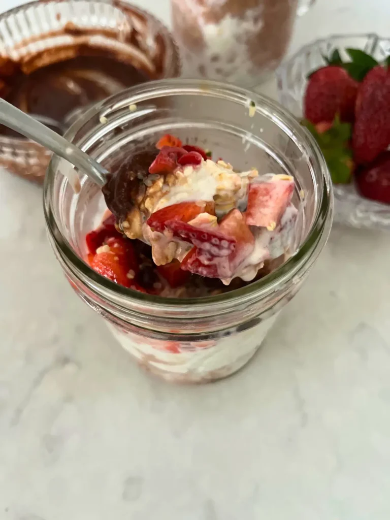 A close-up of a spoonful of chocolate strawberry overnight oats with a bowl of healthy dark chocolate date sauce in the background.