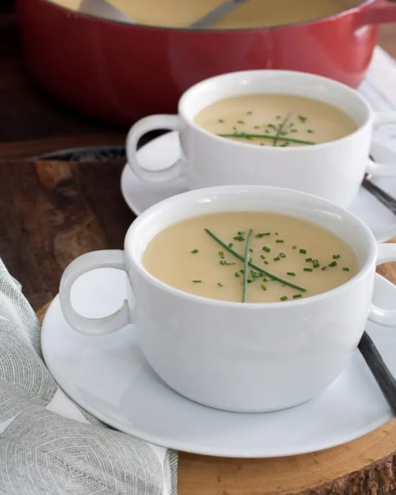 No cream and leek soup in two small cups with saucers on a dining table.