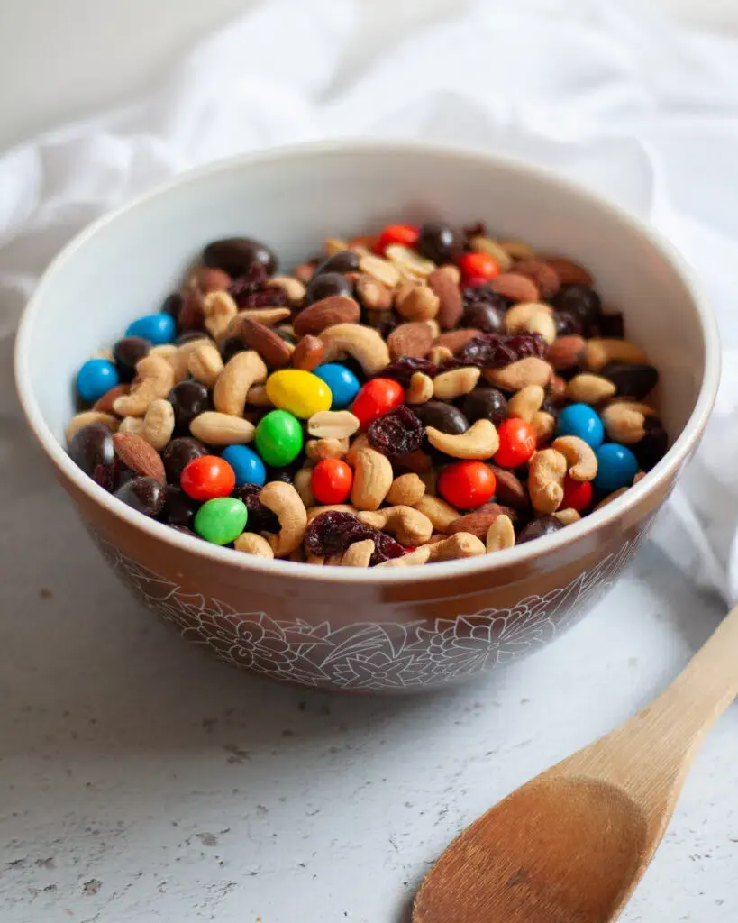 A bowl of DIY trail mix with M&Ms, nuts, and raisins on the counter.