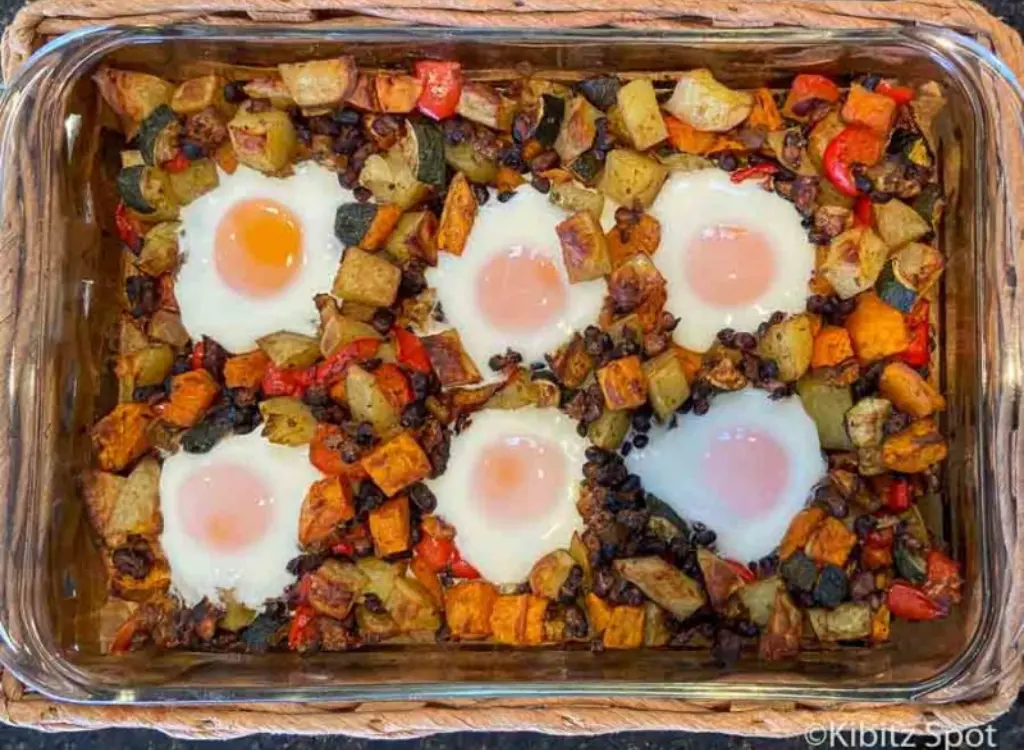 A medley of potatoes and vegetables topped with fried eggs in a baking dish.