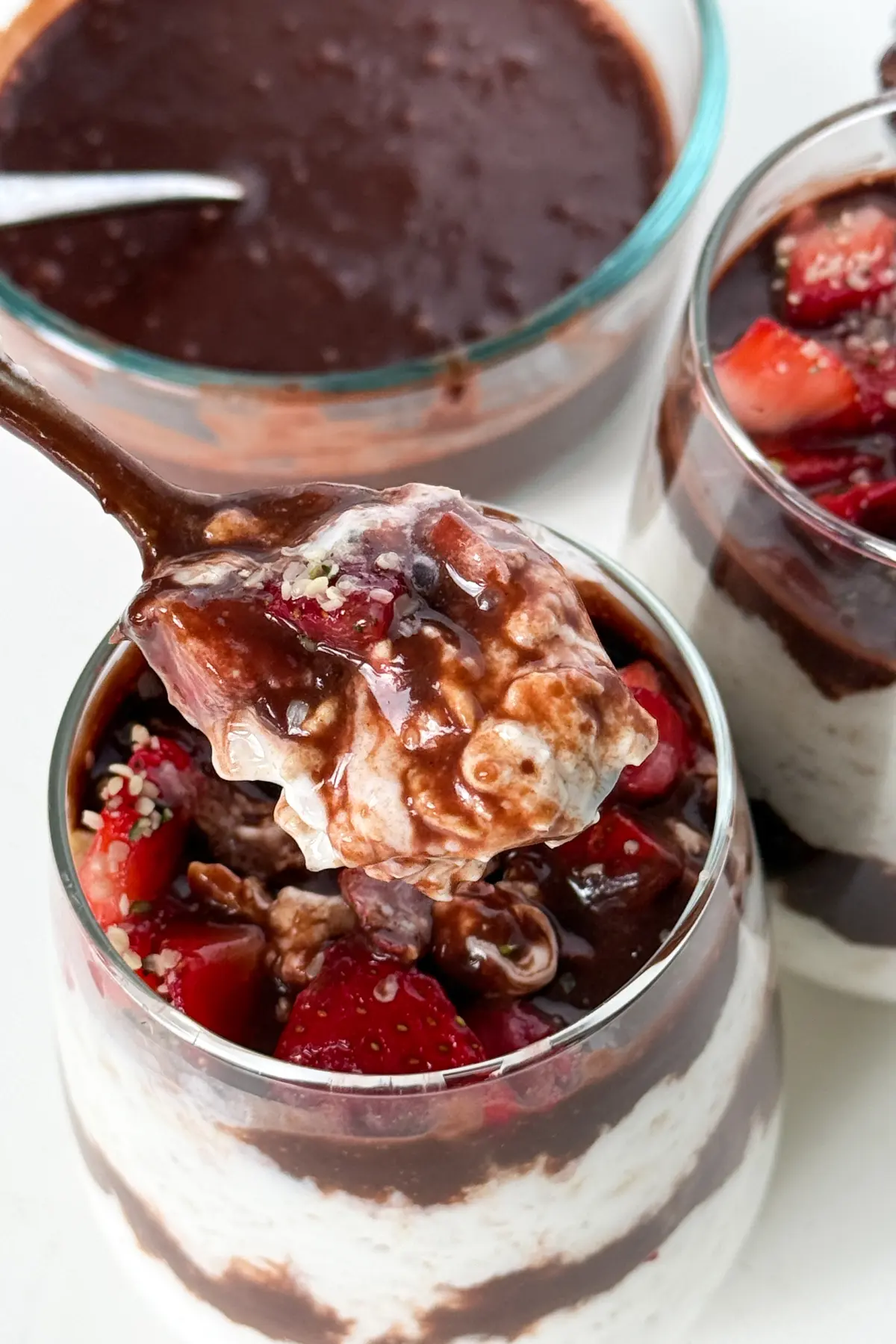 A spoonful of dark chocolate overnight oats with strawberries with a glass in the background.