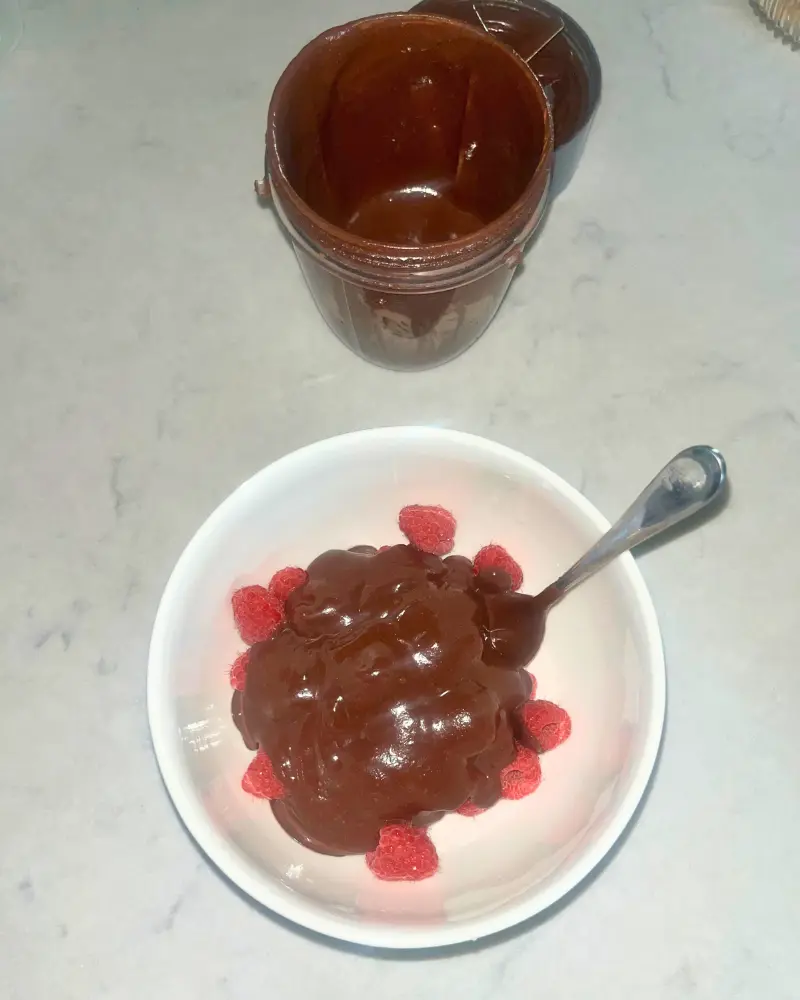 A bowl of raspberries covered in dark chocolate date sauce on a counter.
