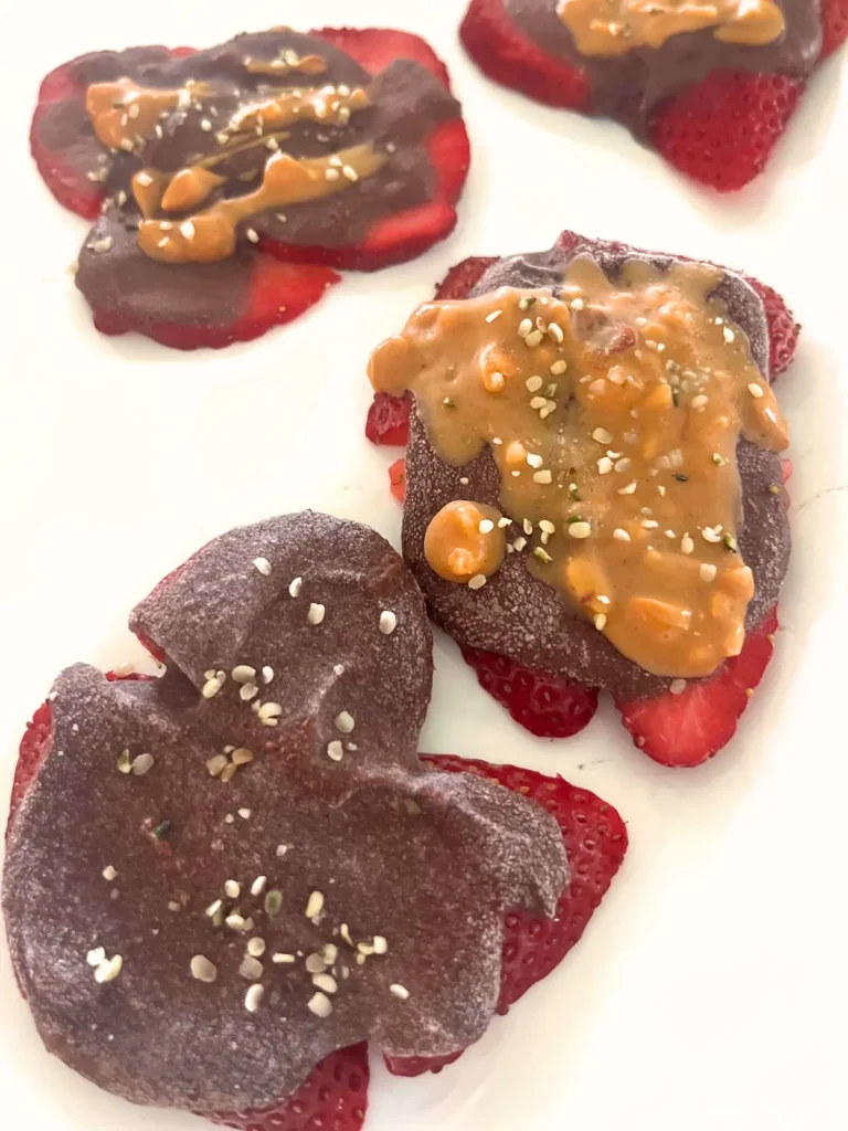 Dark chocolate strawberry bark pieces on a white platter - some drizzled with peanut butter.