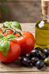 Fresh Roma tomatoes, kalamta olives and a bottle of olive oil on a counter.