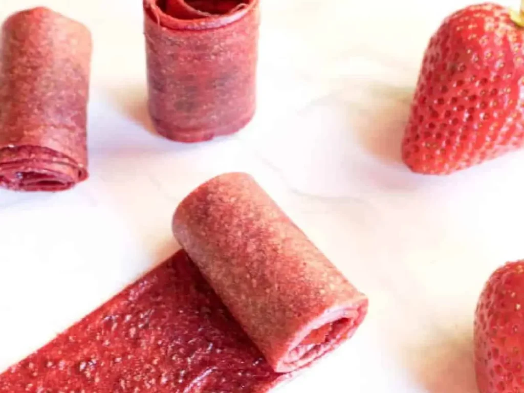 Strawberry fruit roll ups on the counter next to some whole strawberries.