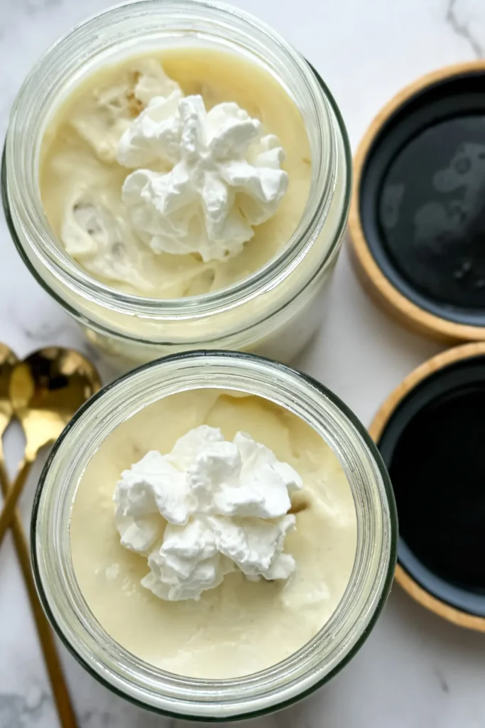 A birds-eye view of banana pudding in jars topped with whipped cream next to two gold spoons.