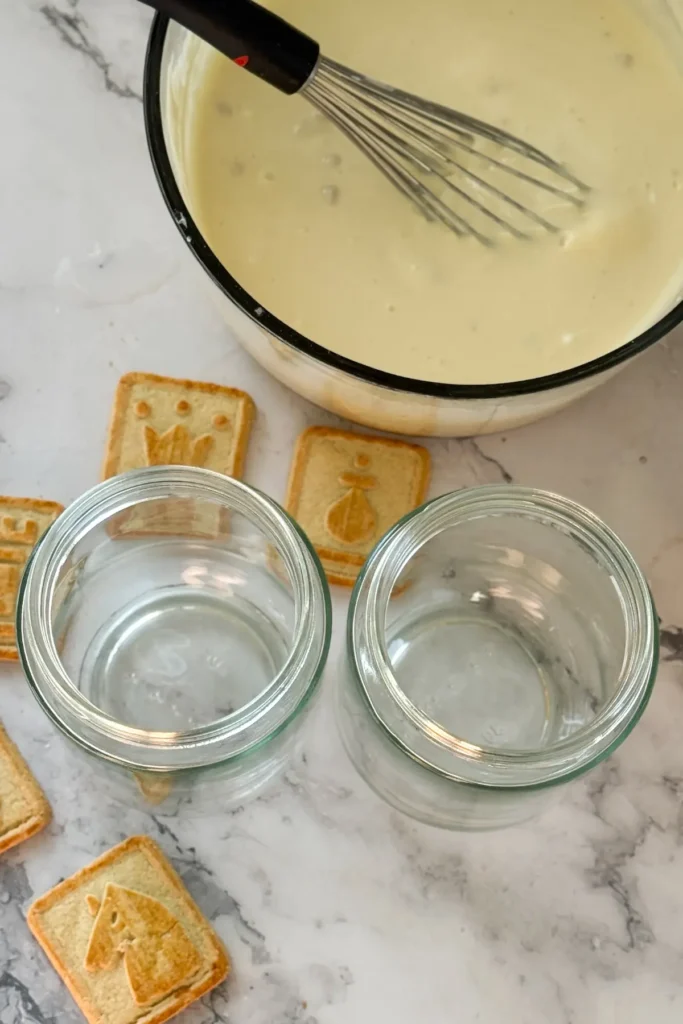 A large bowl of pudding with a whisk in it next to two empty jars.
