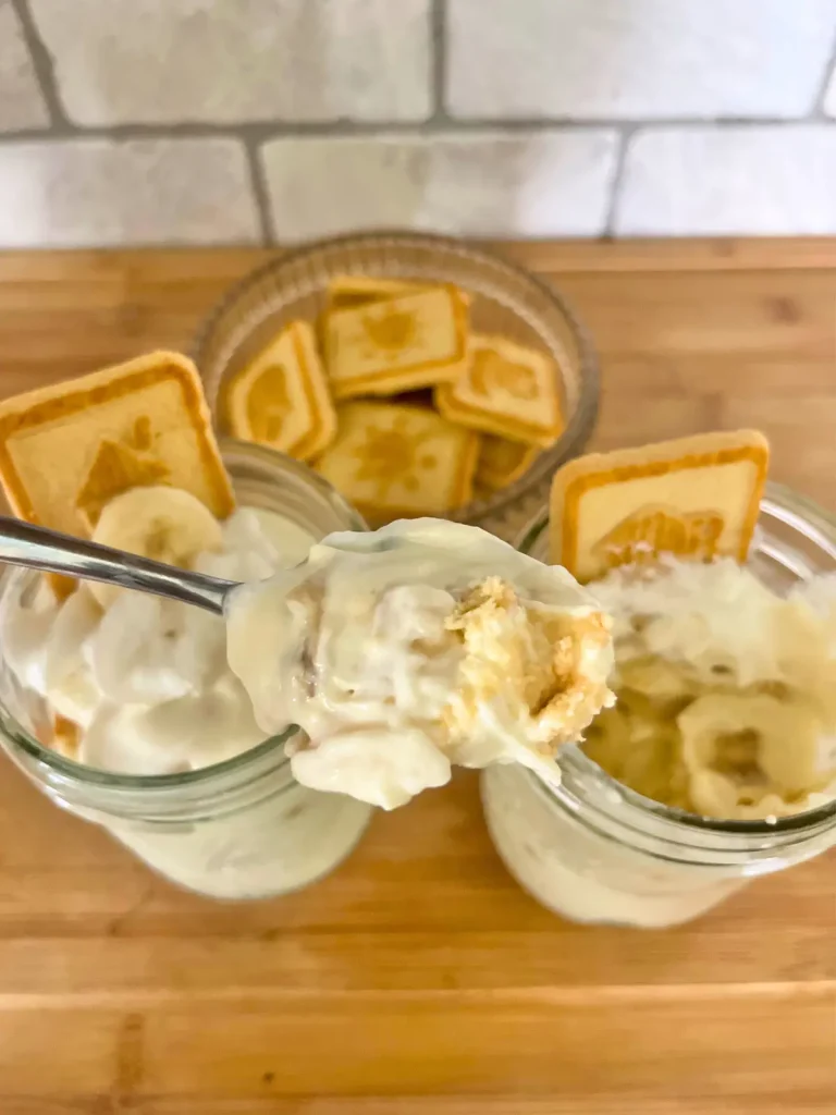 A large spoonful of high protein banana pudding with two jars in the background and a bowl of chessmen cookies.