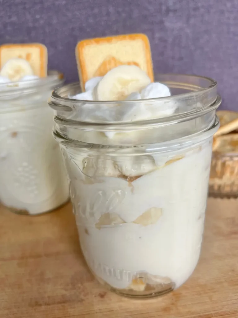 A close-up sideview of a mason jar with high protein banana pudding garnished with a chessmen cookie.
