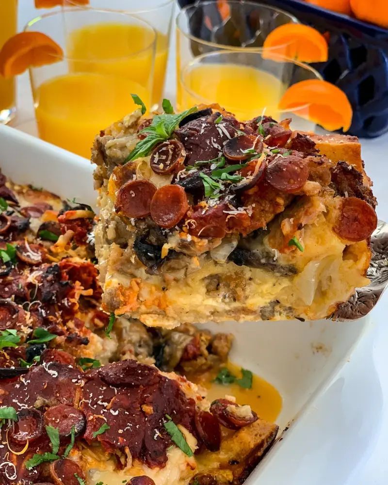 A high protein pizza breakfast casserole with a spatula picking up a large slice from a baking dish.