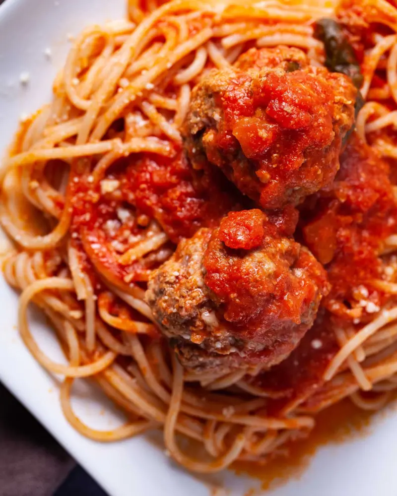 Healthy Italian meatballs served over spaghetti and tomato sauce on a white plate.