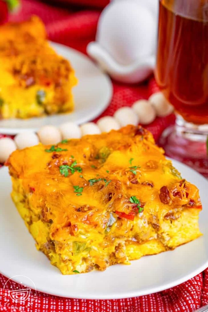 A slice of overnight breakfast casserole on a white plate on a table.
