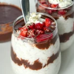 Two galsses of overnight oats layered with dark chocolate date sauce and diced strawberries next to a bowl of date sauce.