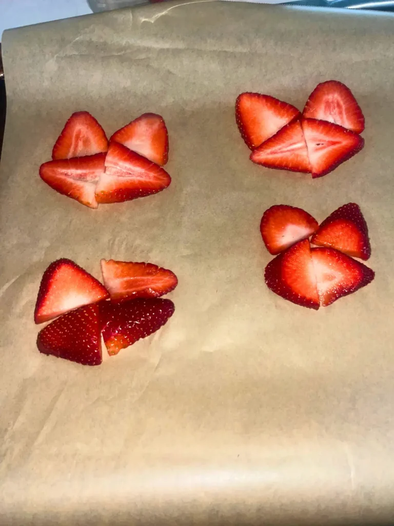 Arranging the thin cut strawberry slices in a circle so they are touching on a parchment lined baking sheet.
