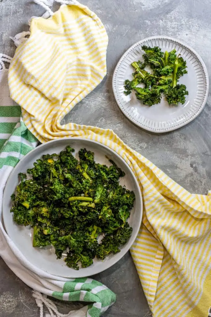 Two plates of kale chips on a counter next to a yellow towel.