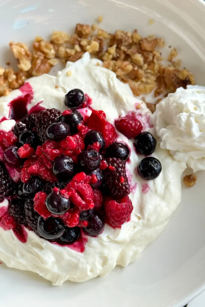 A Greek yogurt cheesecake yogurt bowl topped with mixed berries and chopped nuts.
