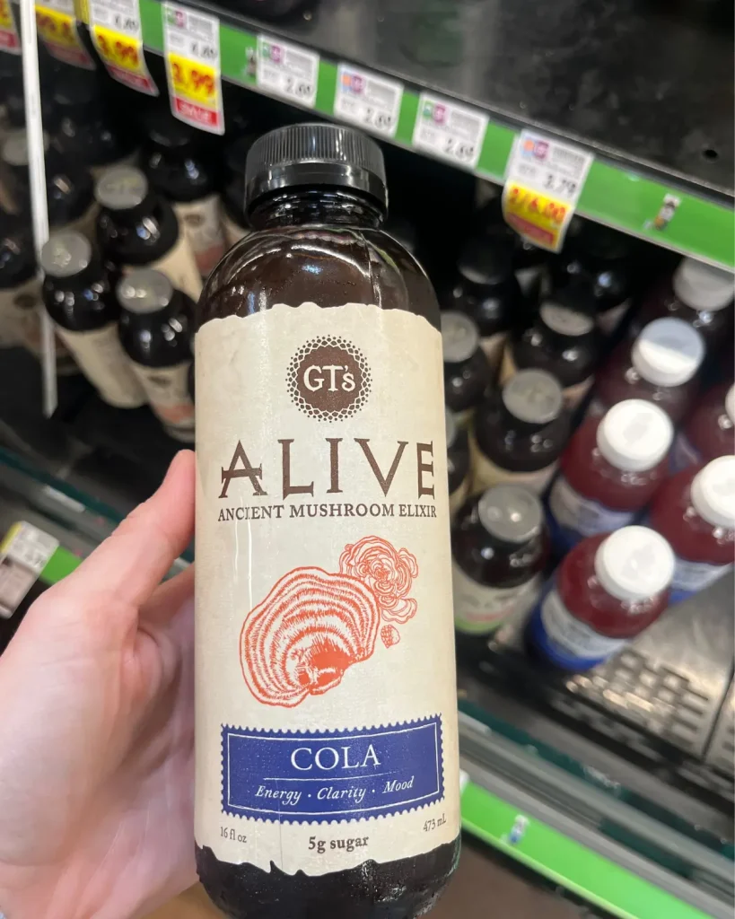 Someone holding a bottle of Alive Mushroom Elixir with other functional beverages in the background.