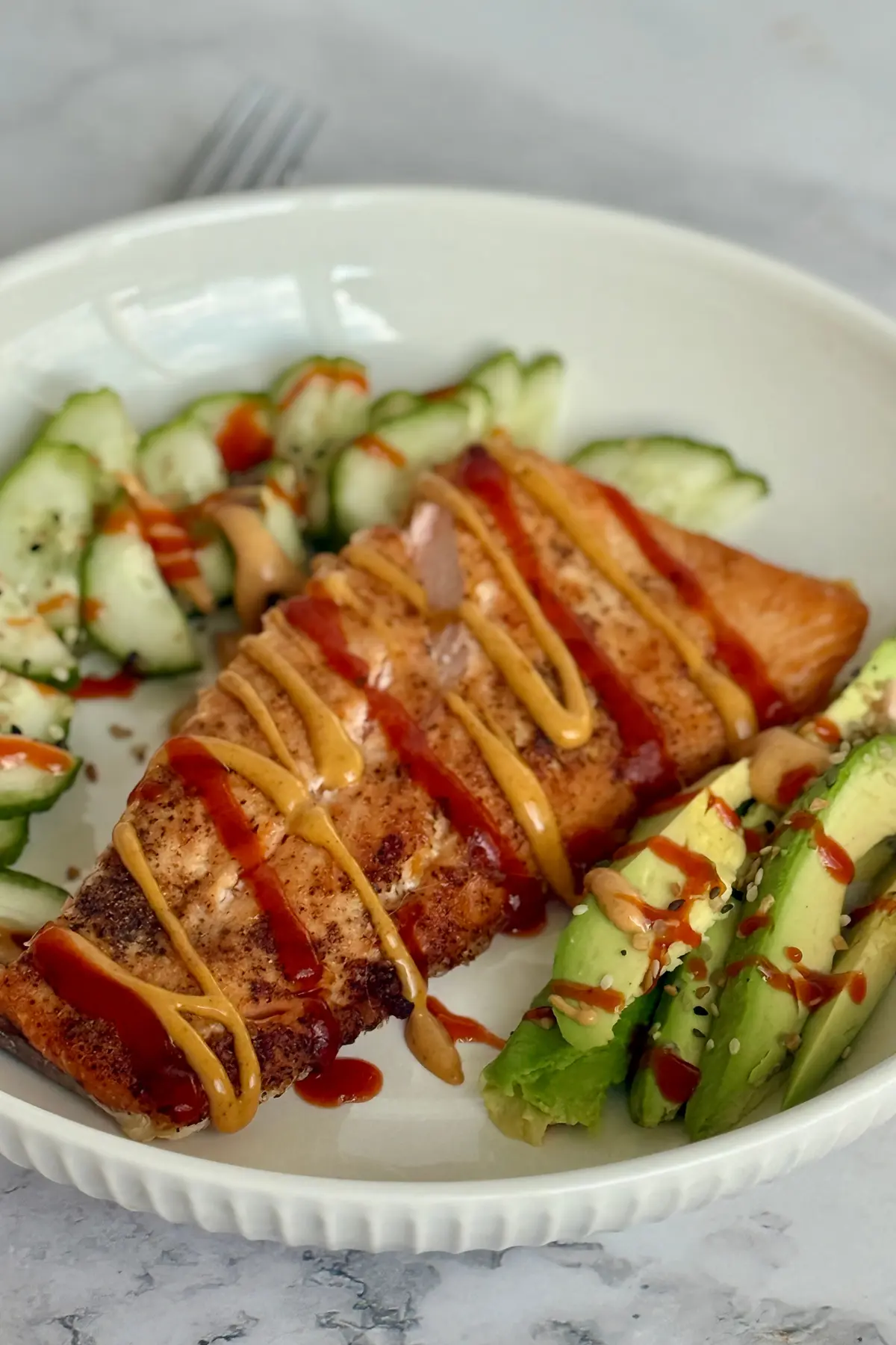 A air fried salmon filet on a plate next to avocado and cucumber slices.