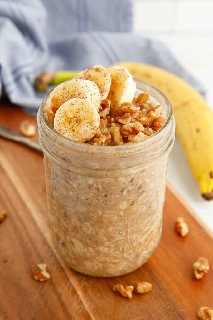Overnight oats topped with bananas and chopped walnuts in a glass jar on a wooden cutting board.