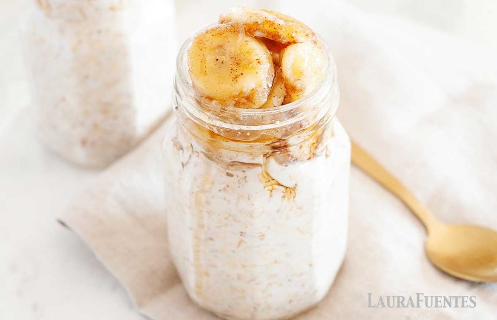 Overnight oats topped with caramelized bananas in a clear glass jar on a table.