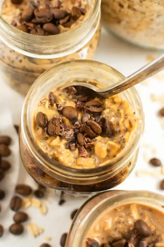 Coffee overnight oats in mason jars, one with a spoon in it.
