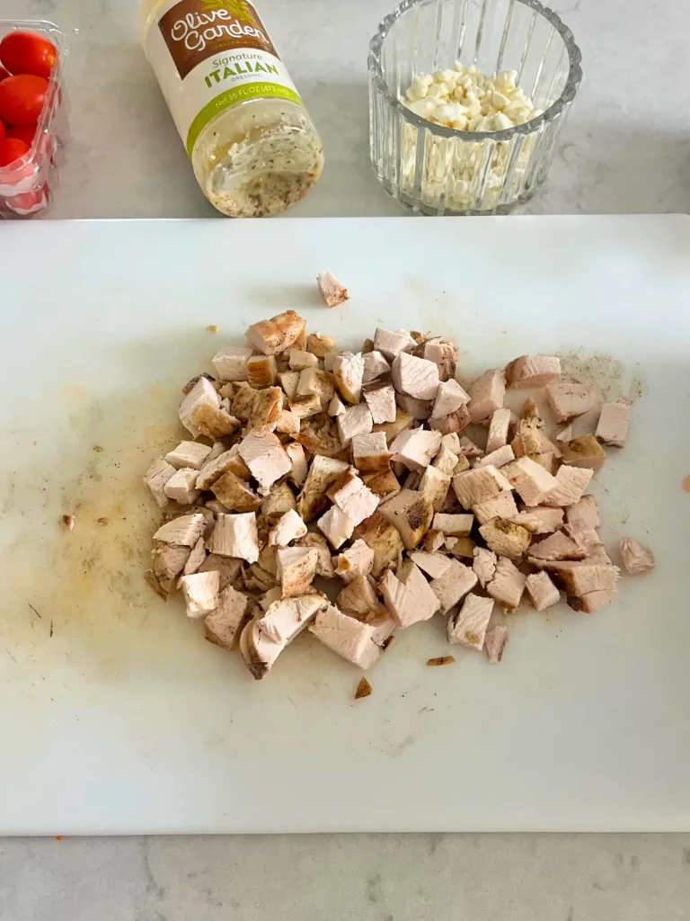 Grilled chicken breast diced up into bite size pieces on a white cutting board.