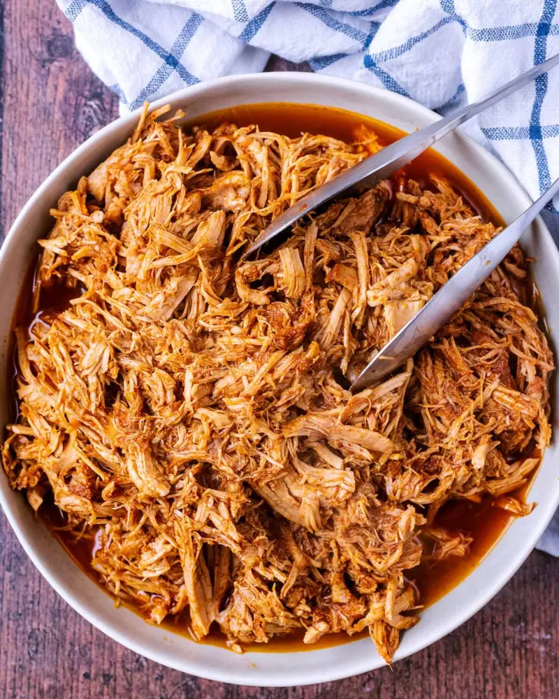 Pulled pork that is shredded in a bowl with tongs.