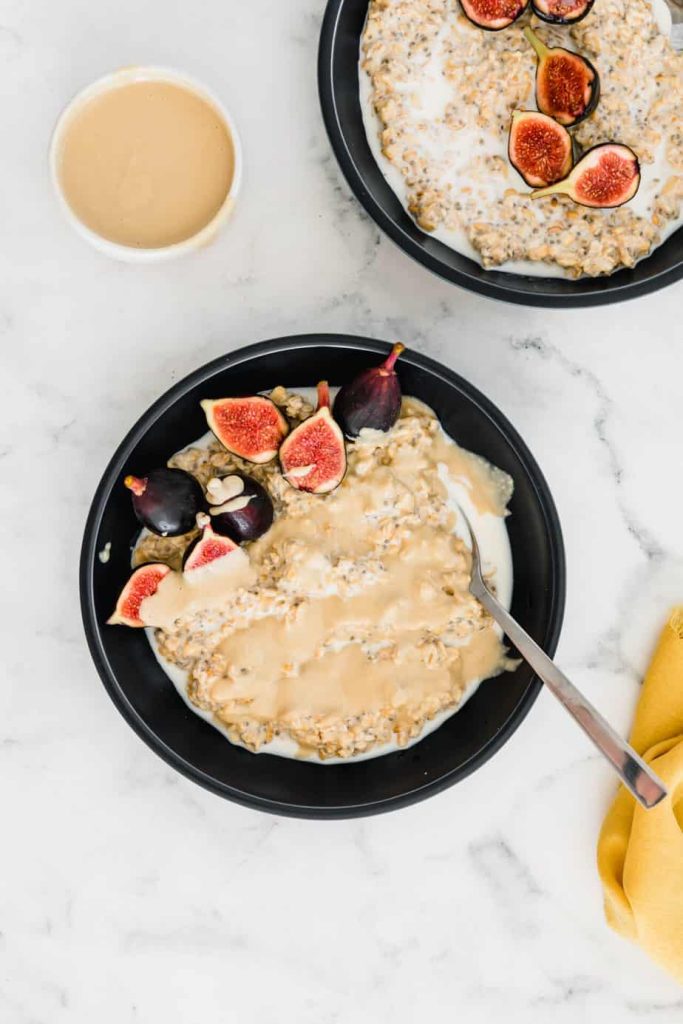 Overnight oats in a bowl topped with tahini and figs on a table.