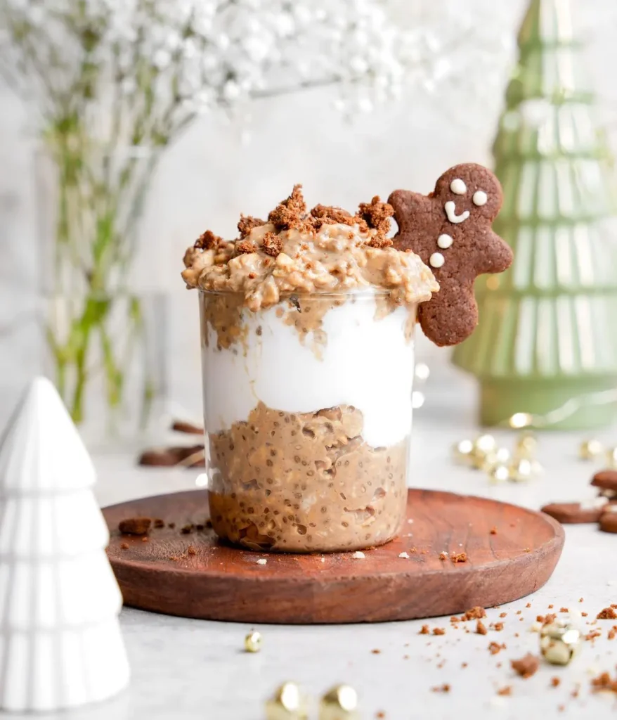 Overnight oats topped with gingerbread and a gingerbread man cookie on a counter decorated for Christmas.