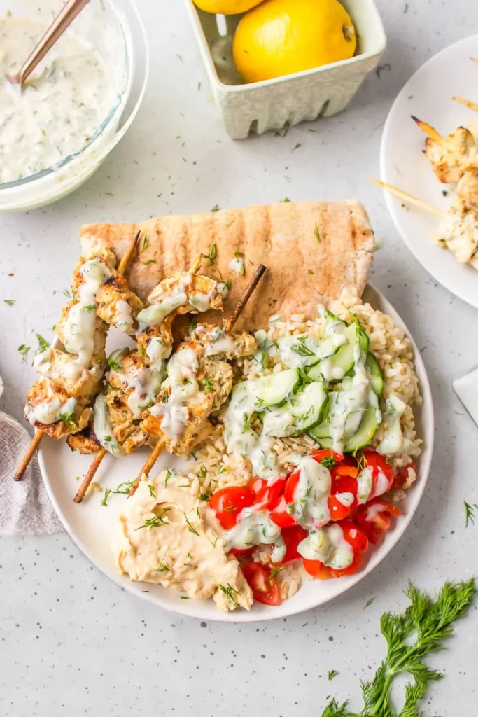 Greek chicken skewers with pita bread, rice, and fresh tomatoes on a plate on the dining table.