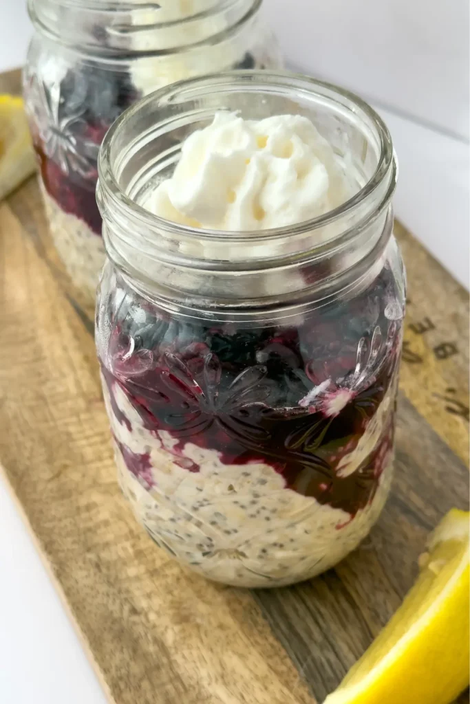 A mason jar of kefir overnight oats topped with mixed berries and whipped cream on a wooden cutting board.